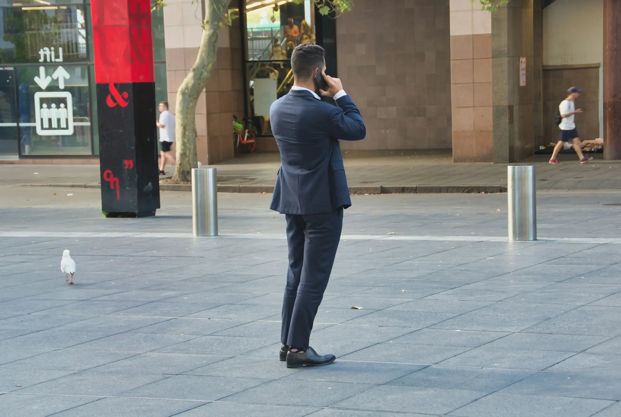 Business owner on a phone call in a city plaza lined with commercial premises in Sydney