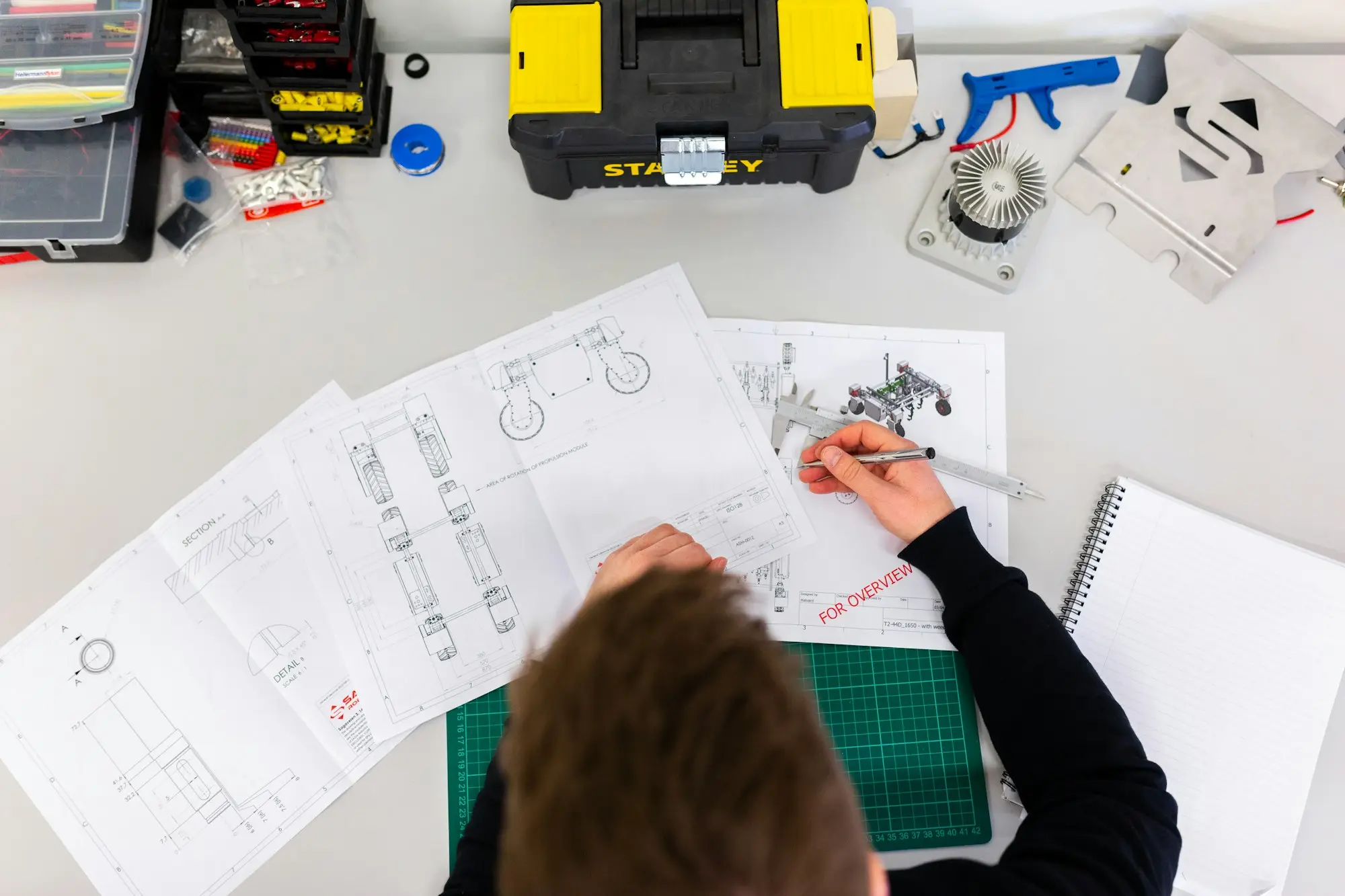 Engineer sketching a prototype design at a workbench covered in technical drawings