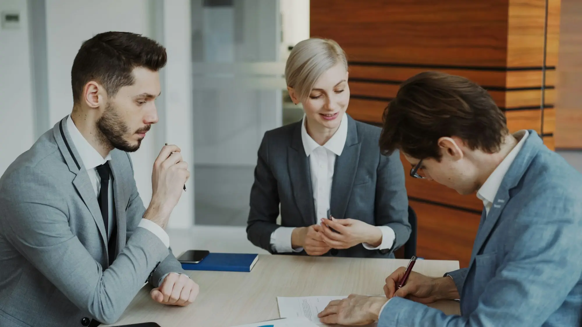 Business owners signing settlement documents with an adviser at a meeting table