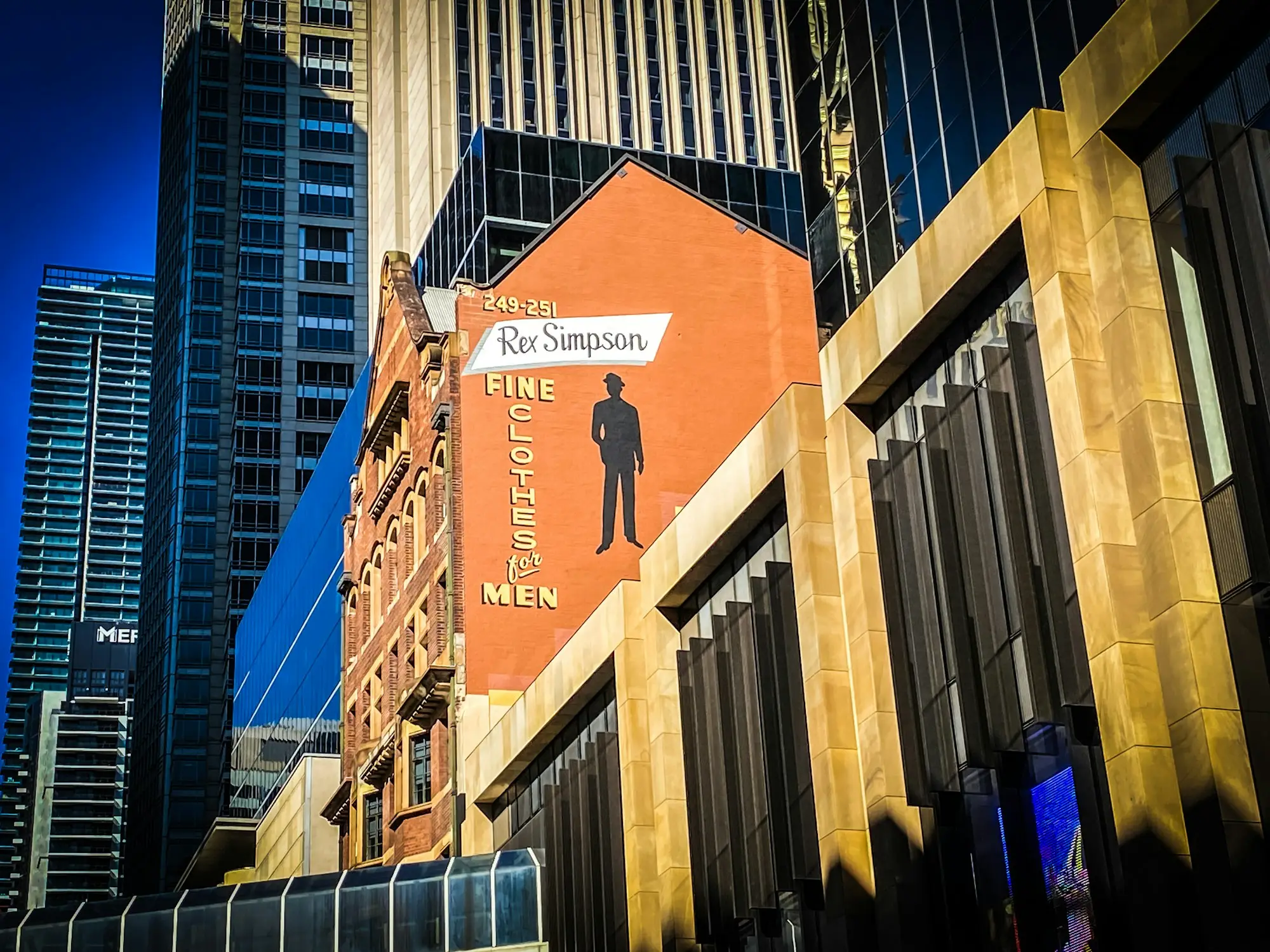 Heritage commercial building with a painted mural beside glass towers on George Street, Sydney